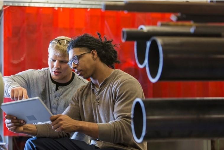 Two people looking at a laptop in a manufacturing facility.